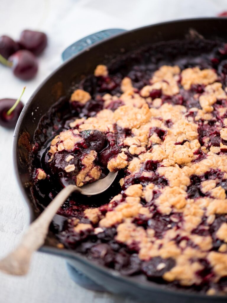 fresh cherry crisp in a cast iron skillet being scooped with a spoon