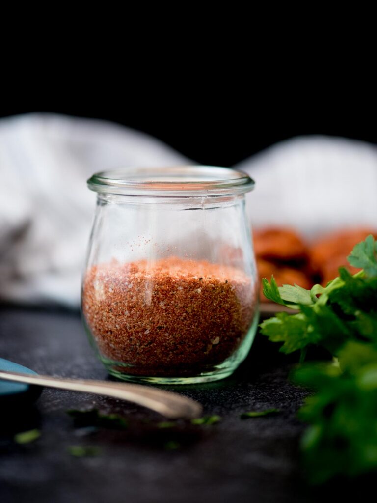 Half a glass jar of chicken seasoning with fresh herbs laying next to it
