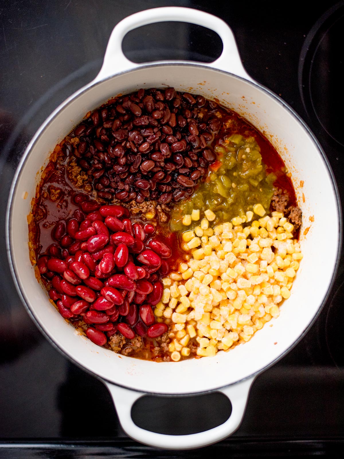 Dutch oven with corn, black beans, kidney beans and corn added inside.