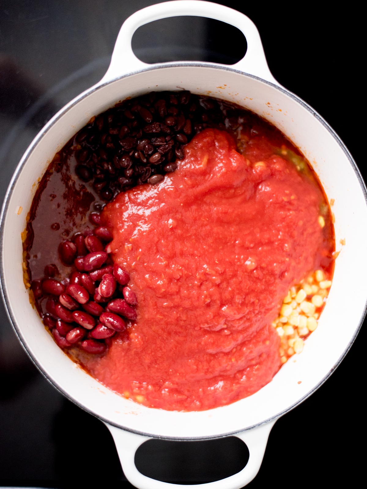 Dutch oven with crushed tomatoes, corn, black beans, kidney beans and corn added inside.