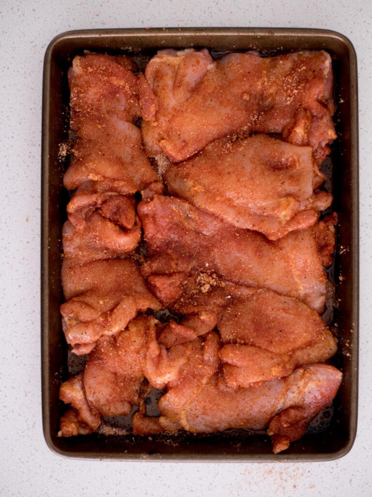 Baking sheet covered with seasoned raw chicken thighs.