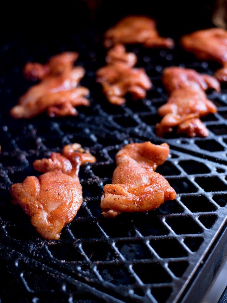 Raw seasoned chicken thighs laying on the grate of a smoker.