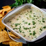 Corn tortilla chips laying around an aluminum pan of smoked queso blanco.
