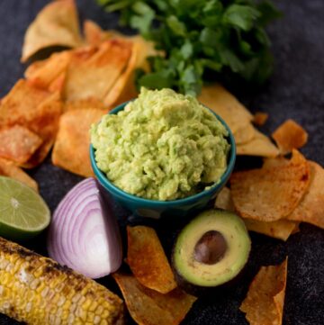 Small bowl of 4 ingredient guacamole dip with tortilla chips around the bowl and a half avocado and red onion.
