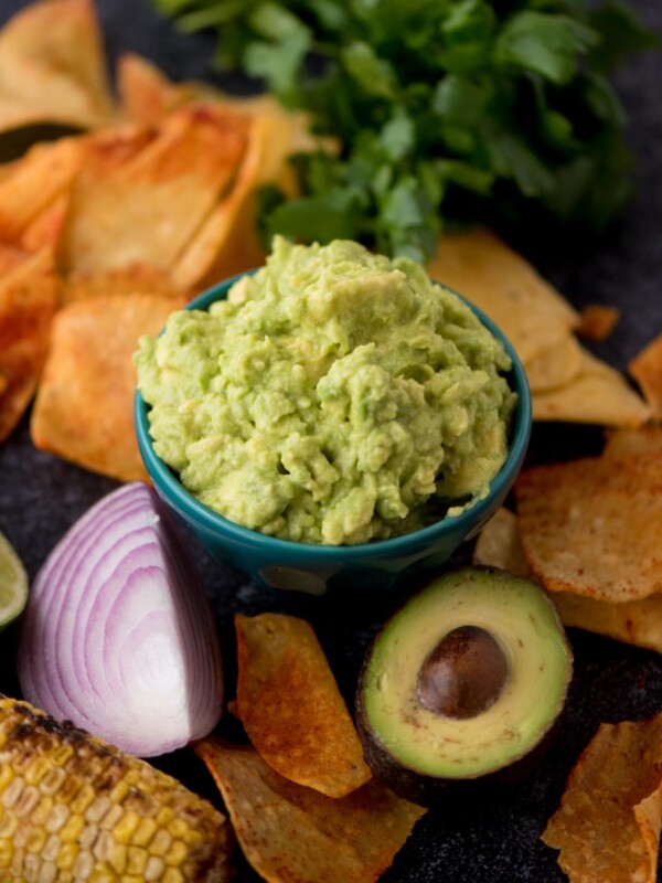 Small bowl of 4 ingredient guacamole dip with tortilla chips around the bowl and a half avocado and red onion.