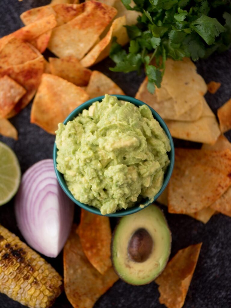 Top view of 4 ingredient guacamole in a bowl with tortilla chips around it and half an avocado and red onion.