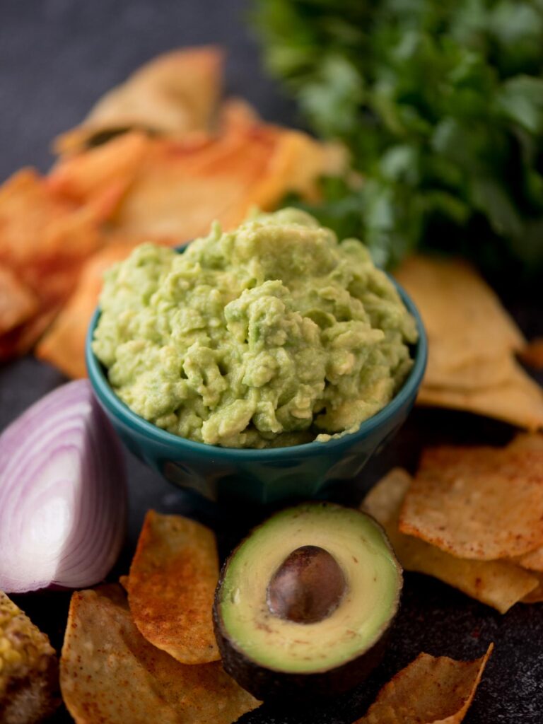 Tortilla chips, half an avocado and red onion next to a small bowl of 4 ingredient guacamole.