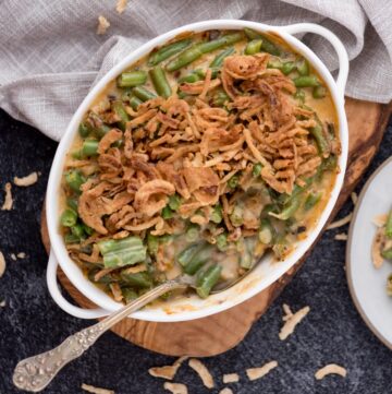 Spoon laying in a baking dish of air fryer green bean casserole topped with french's fried onions.
