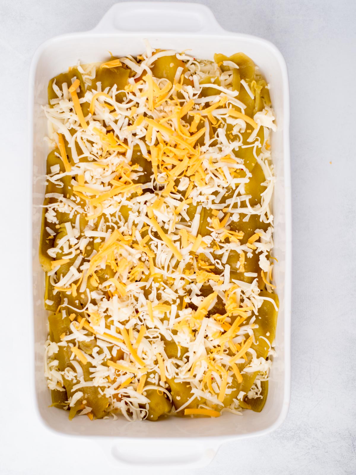 Casserole baking dish with egg mixture, hatch chiles and shredded cheese layered in it.