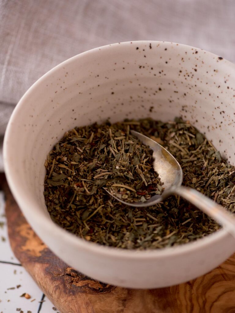 Spoon of homemade italian seasoning in a bowl.