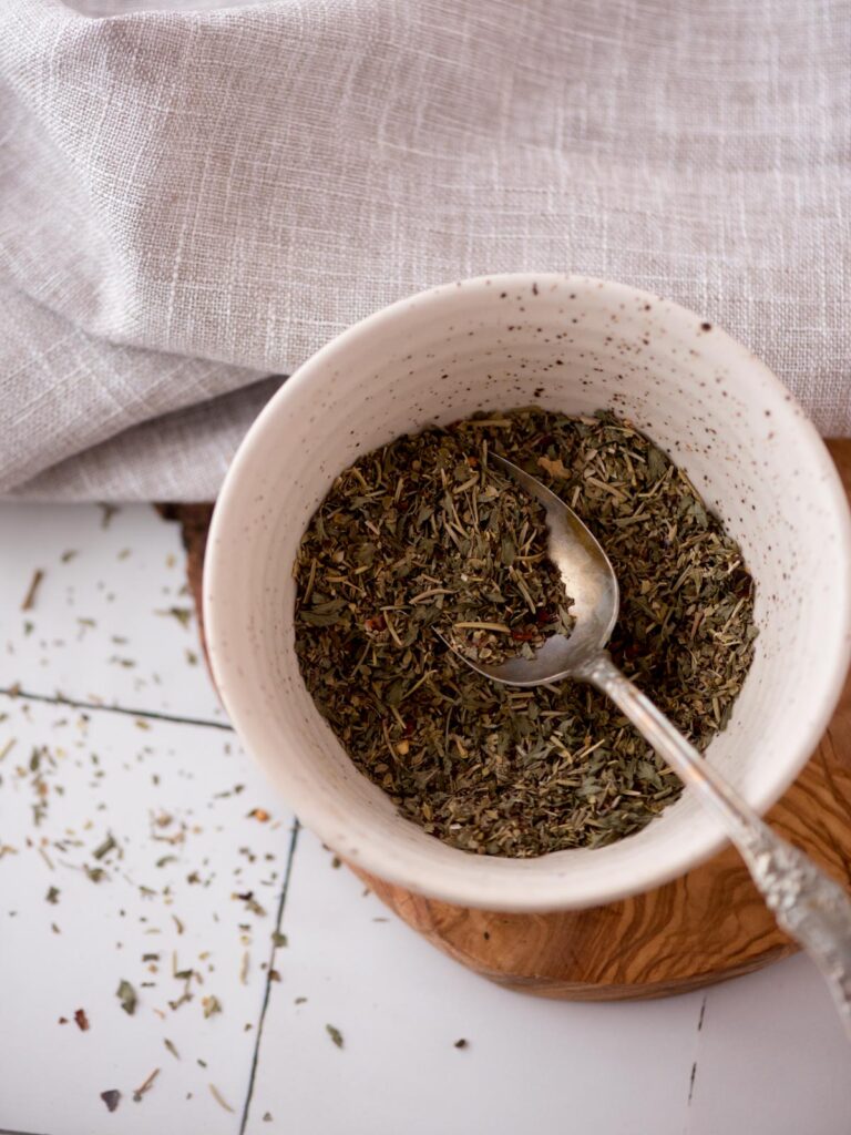 Italian seasonings combined in a small bowl with a teaspoon in it.