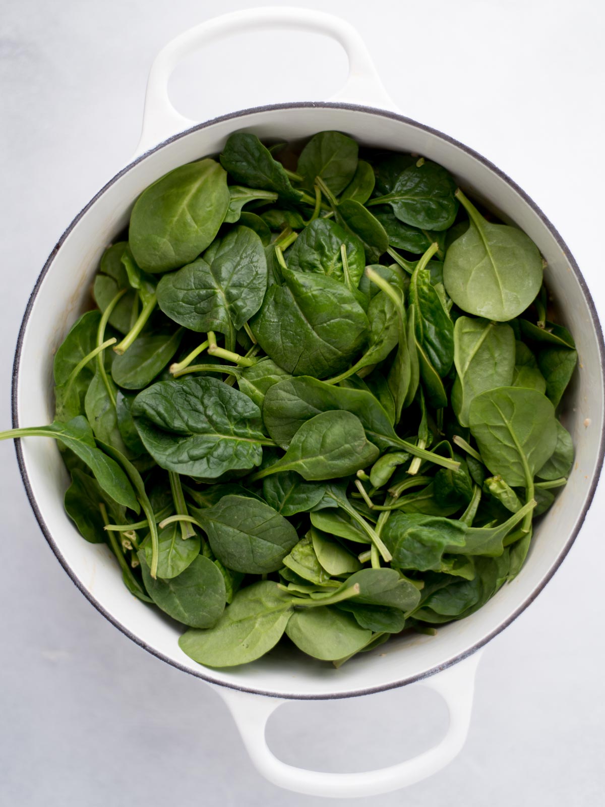 Dutch oven filled with fresh spinach leaves.