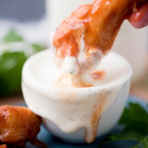 Hand dunking a drumstick into a small bowl of wing stop ranch.