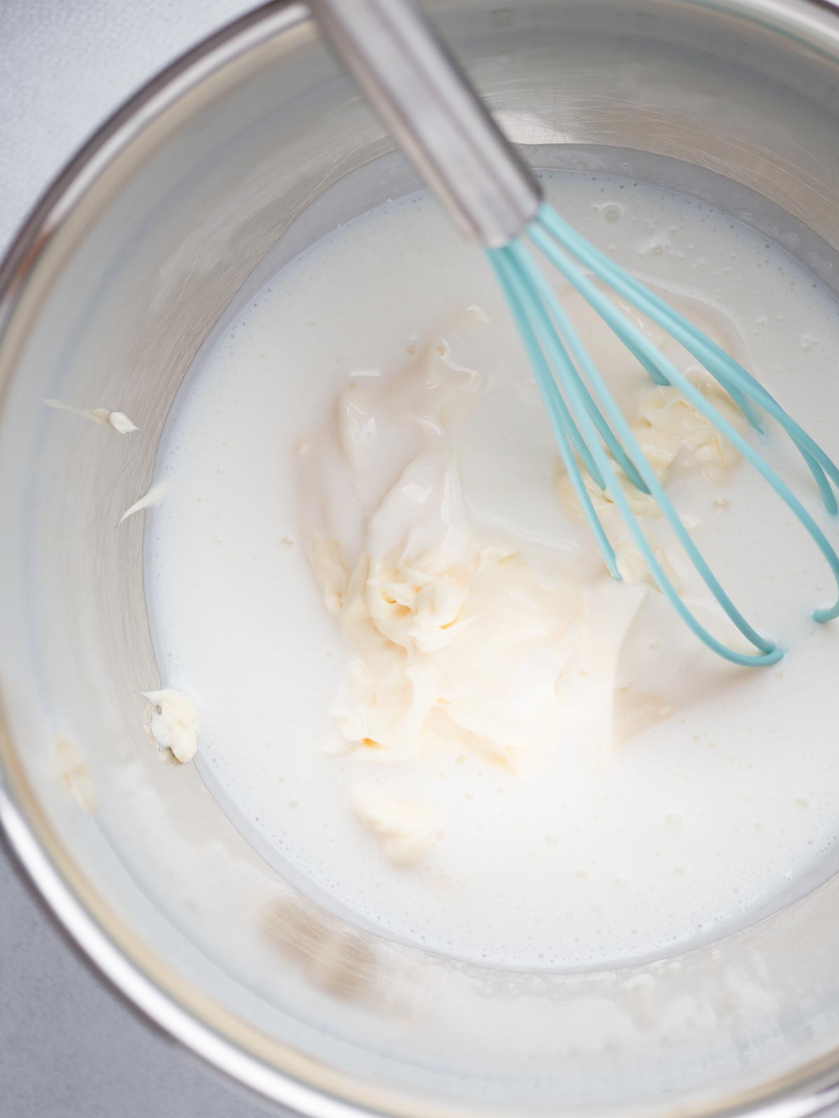 Mixing bowl with buttermilk and mayo measured into the bowl with a whisk propped into it.