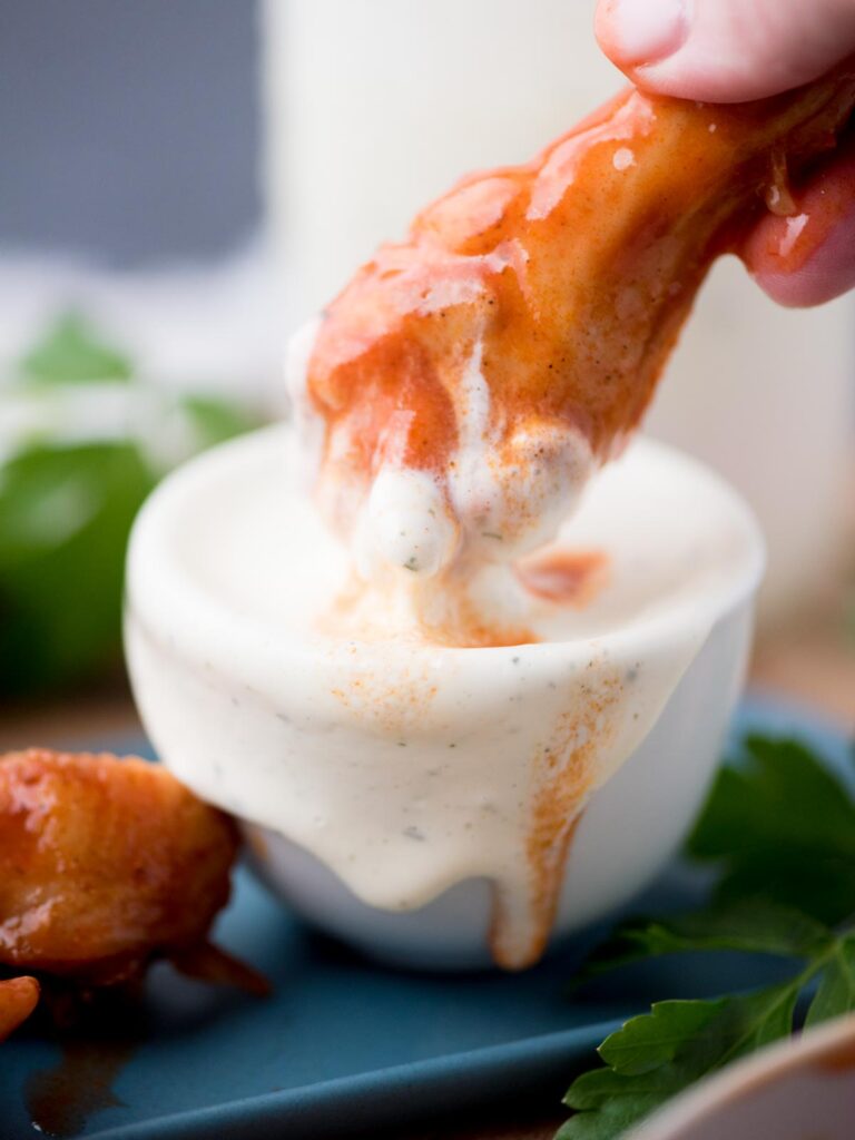 Hand dunking a drumstick in a small bowl of wing stop ranch.