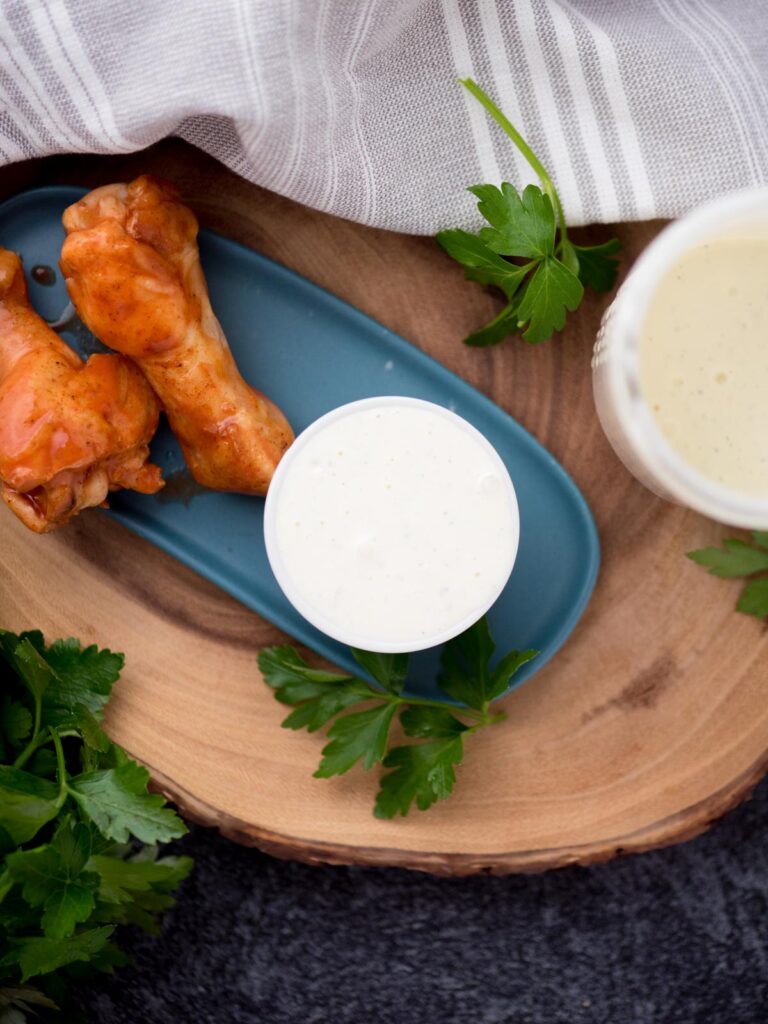 Drumsticks on a plate next to a small bowl of wing stop ranch and cilantro leaves garnished on the side.
