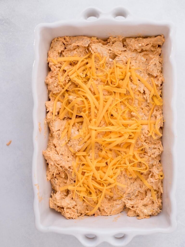 Shredded cheese sprinkled over buffalo chicken mixture in a baking dish.