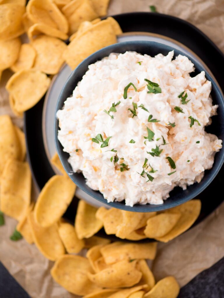 corn dip in a blue bowl sprinkled with chopped parsley surrounded by corn chips