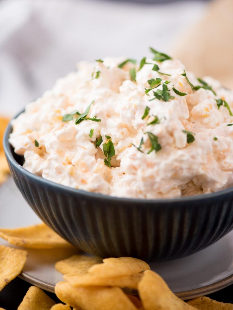 corn dip in a dark blue bowl sprinkled with chopped parsley and surrounded by corn chips