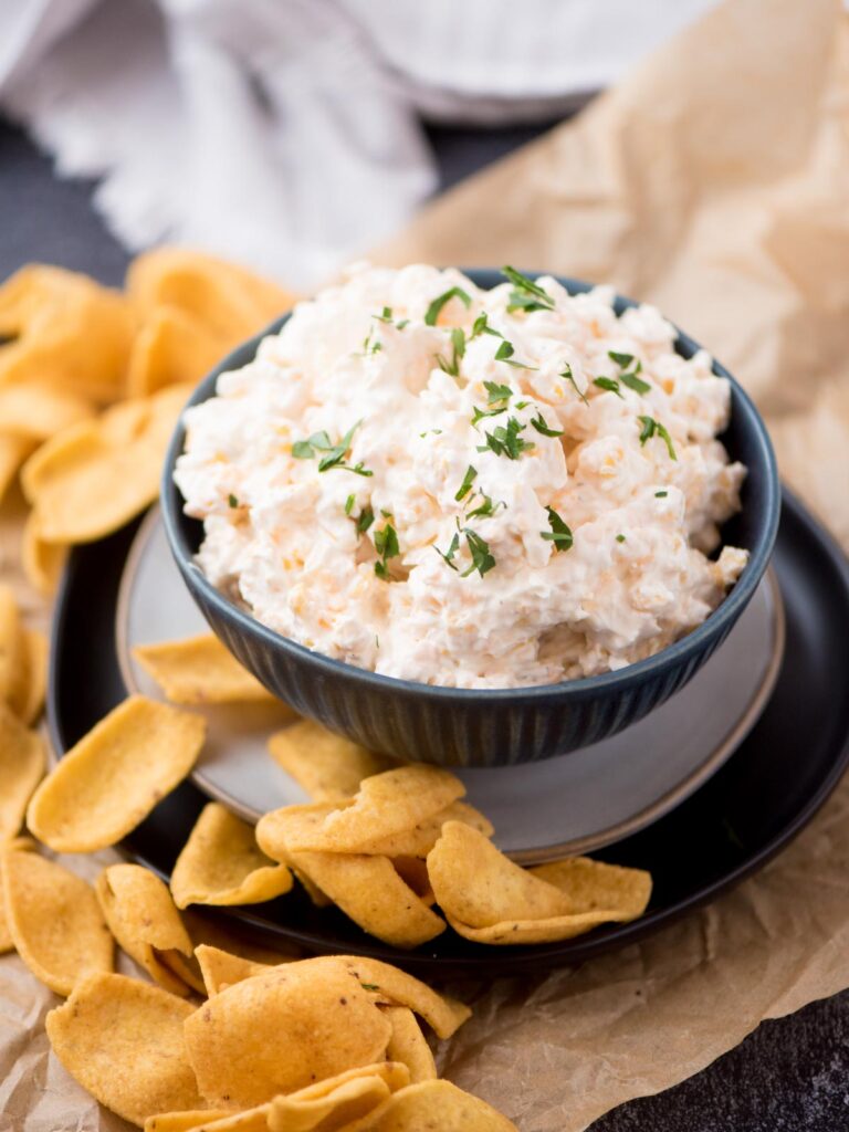 corn dip with cream cheese in a blue bowl topped with chopped parsley surrounded by corn chips
