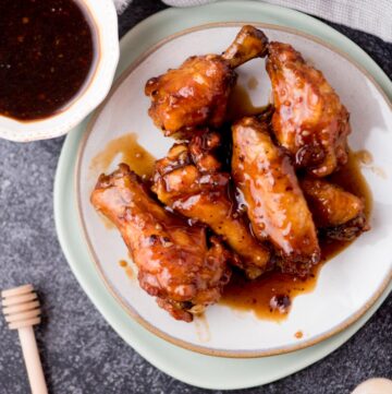 honey garlic chicken wings on a plate covered in sauce with a side of extra sauce in a bowl