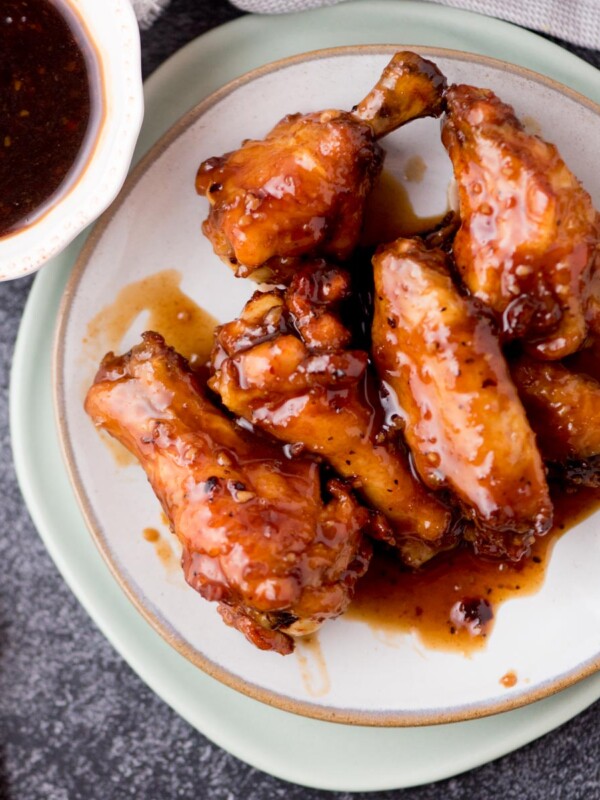 honey garlic chicken wings on a plate covered in sauce with a side of extra sauce in a bowl