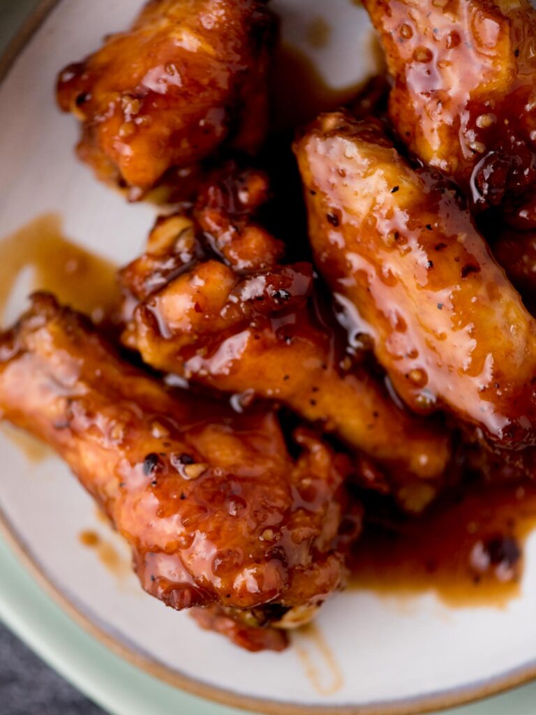 stacked honey garlic chicken wings on a white plate