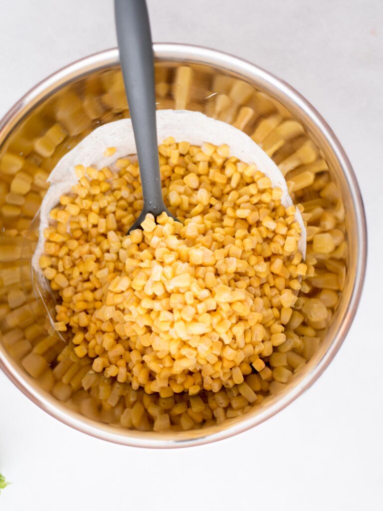 Corn added to the street corn casserole sauce in a mixing bowl.