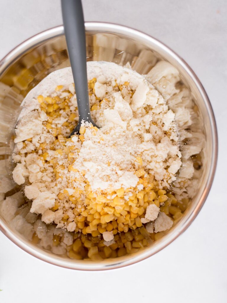 Mixing bowl with corn and cotija cheese inside with a mixing spoon.