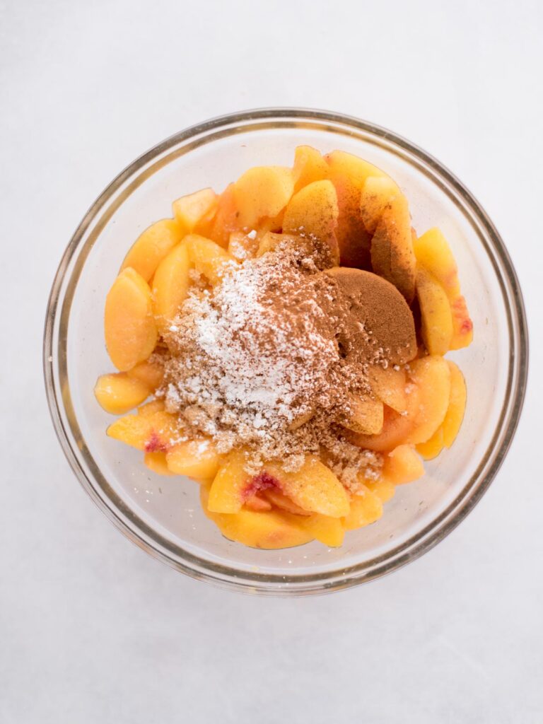 Glass bowl of peaches with brown sugar and seasoning added to the top.