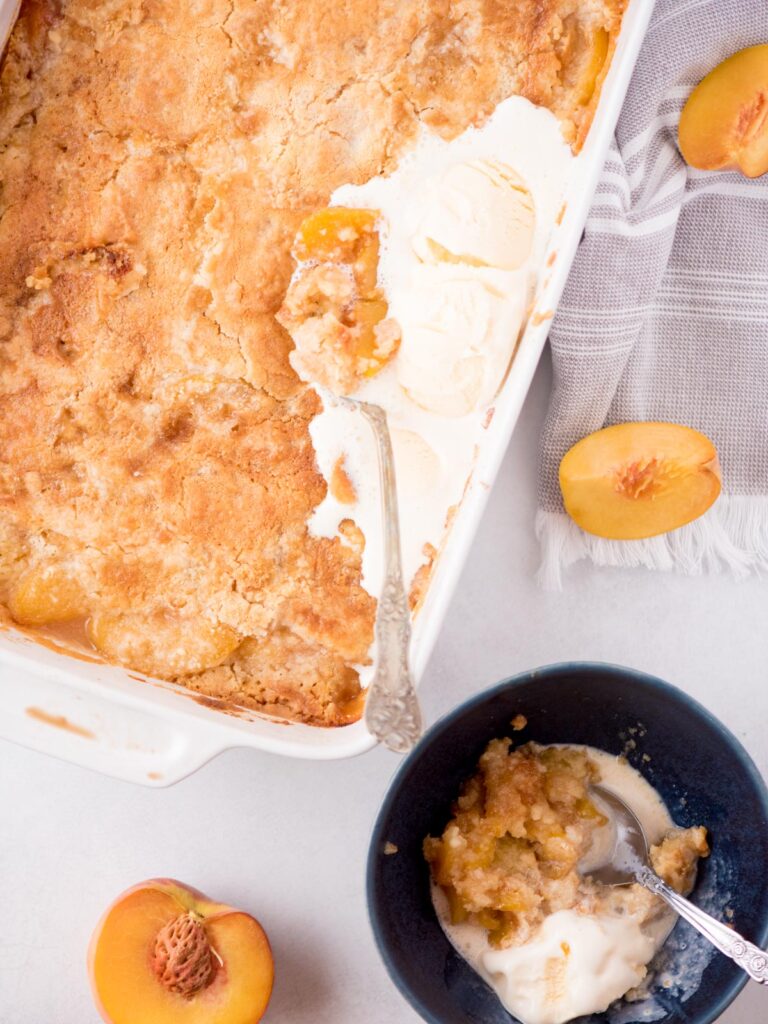 Ice cream melting over peach cobbler with a bowl of partially eaten cobbler and melted ice cream in a bowl.