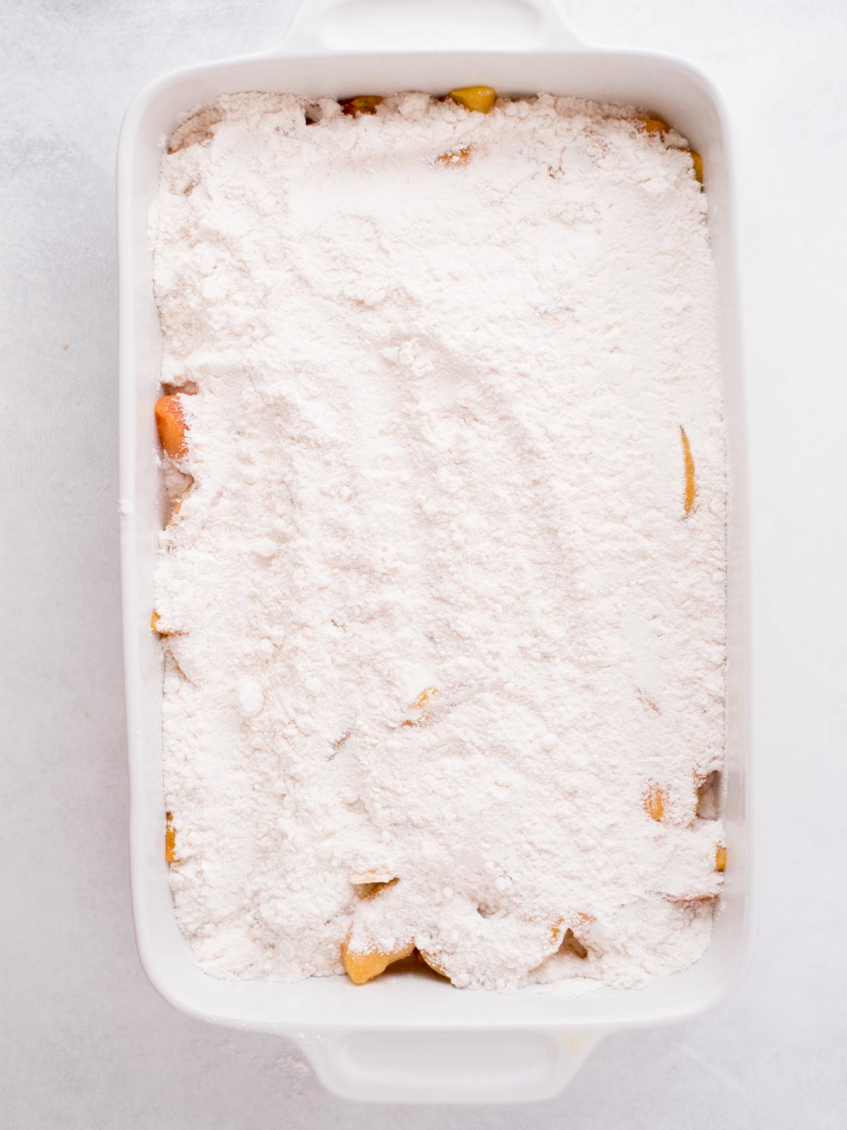 Frozen peaches topped with cake mix in a baking dish.