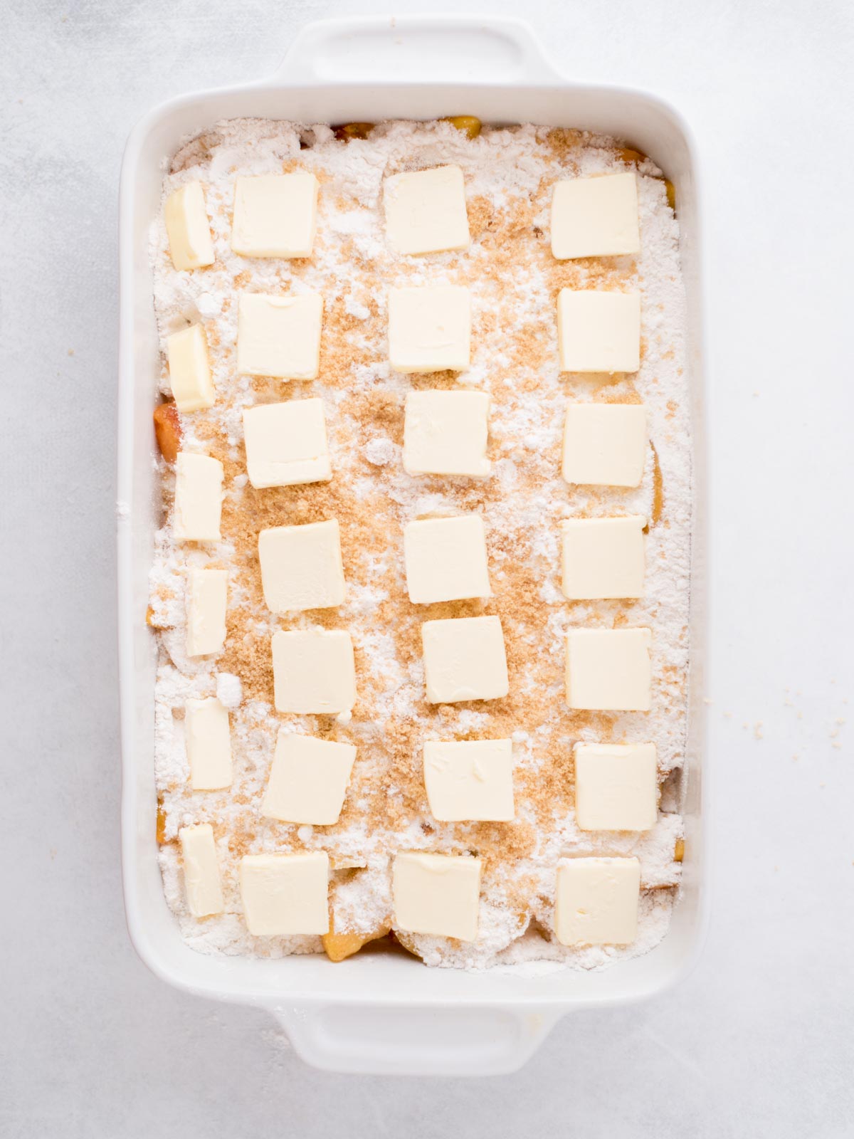 Unbaked peach cobbler in a baking dish with pats of butter arranged over the top.