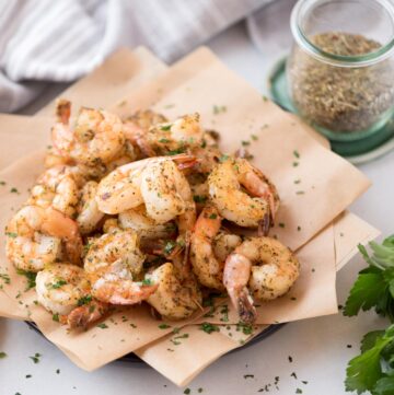 Air fryer frozen seasoned shrimp served on parchment paper covered plate.