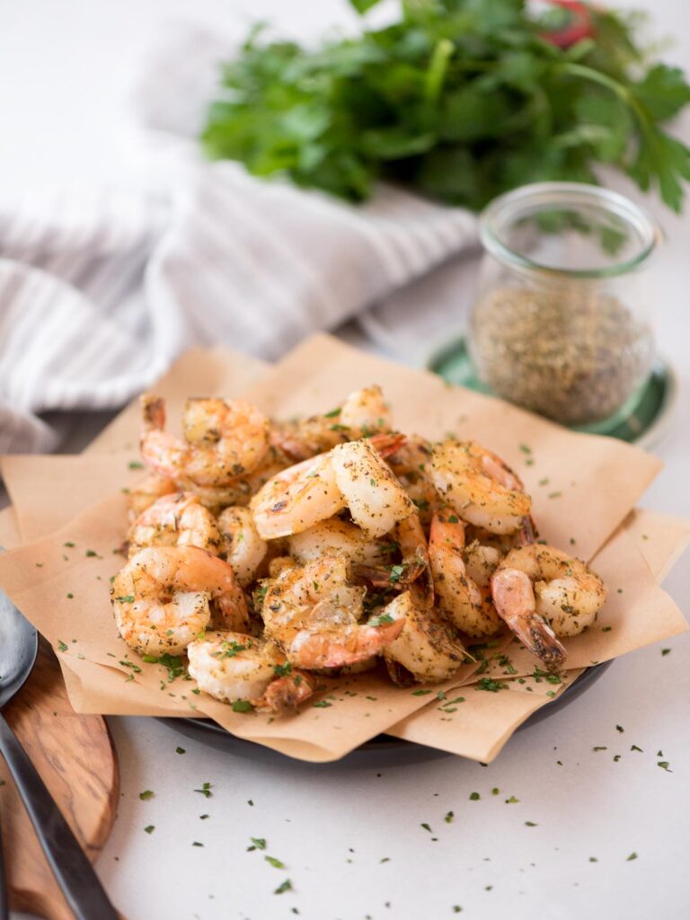 Air fryer frozen seasoned shrimp served on parchment paper covered plate.