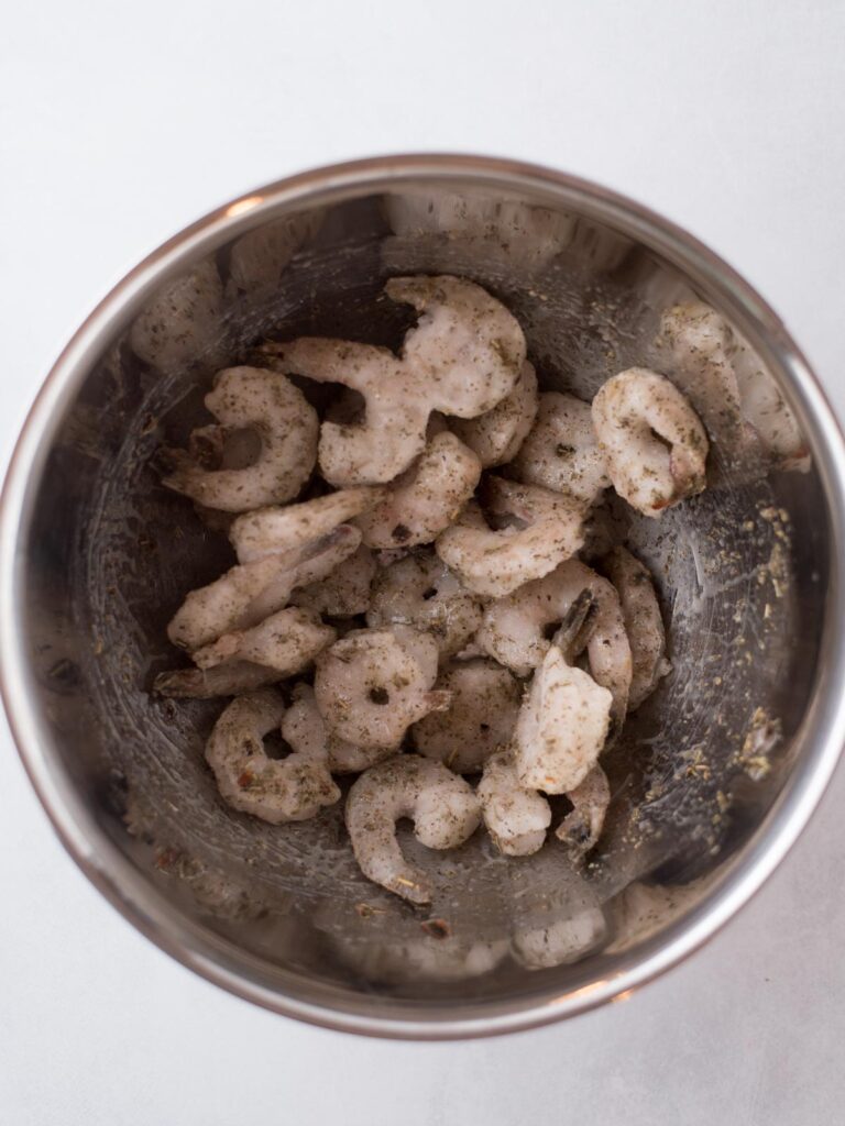 Frozen shrimp inside a mixing bowl covered with oil and seasoning.