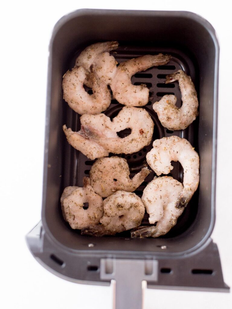 Frozen shrimp laying inside the bucket of an air fryer.