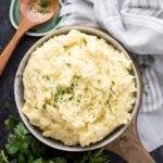 Serving bowl of boursin mashed potatoes with a wooden spoon laying next to it.