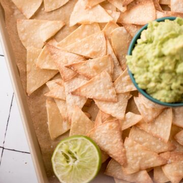 Delicious homemade baked chips on a serving tray with a side of guacamole and a squeeze lime half.