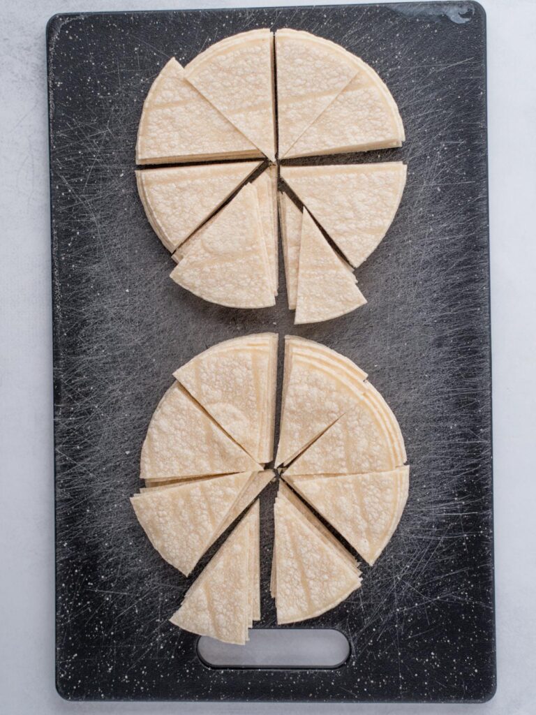 Cutting board with stacks of corn tortillas cut into triangles in preparation for making homemade chips.