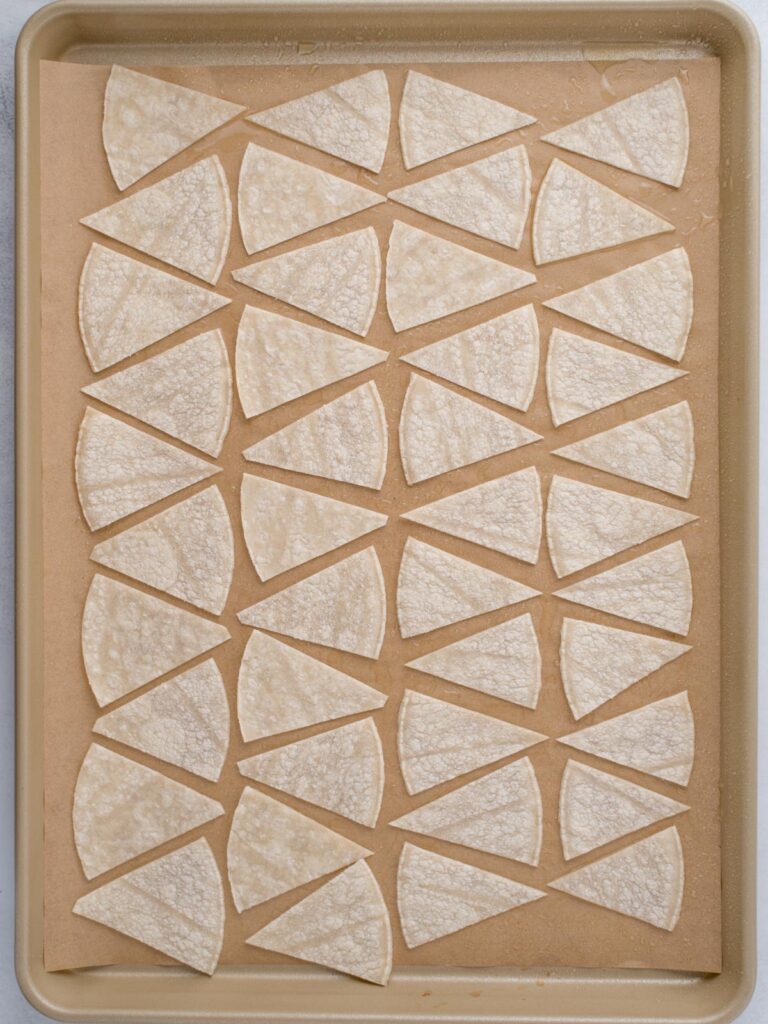 Corn tortillas cut into triangles and arranged on a sheet pan ready to bake.
