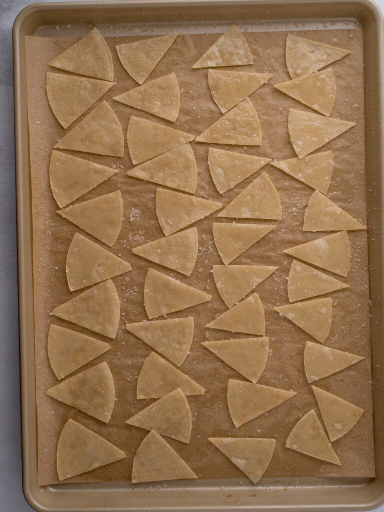 Salted and oiled corn tortillas cut into triangles on a baking sheet ready to bake.