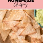 A baking sheet holding a serving of tortilla chips salted and a partial view of guacamole with a squeezed lime half garnish on the side with text overlay the best homemade chips.