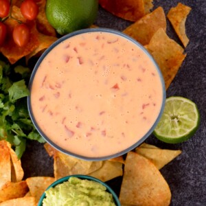 Tortilla chips surrounding a bowl of velveeta queso with a lime wedge.