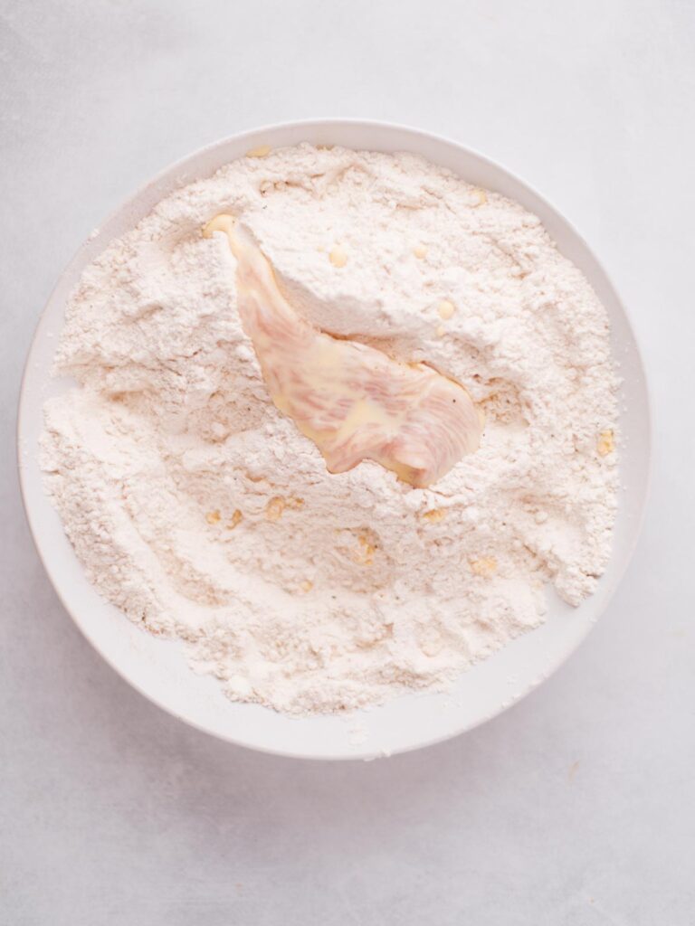 Chicken dipped in egg mixture and placed in seasoned flour bowl to become coated.