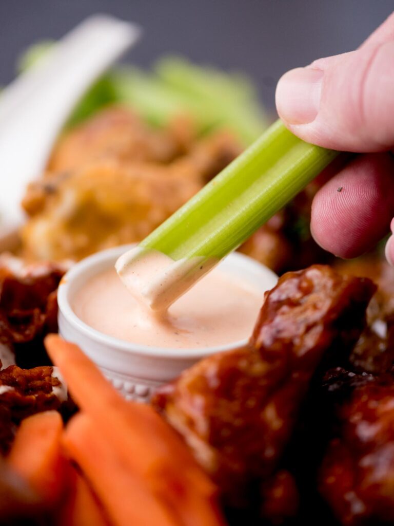 a celery stick being dipped in buffalo ranch sauce