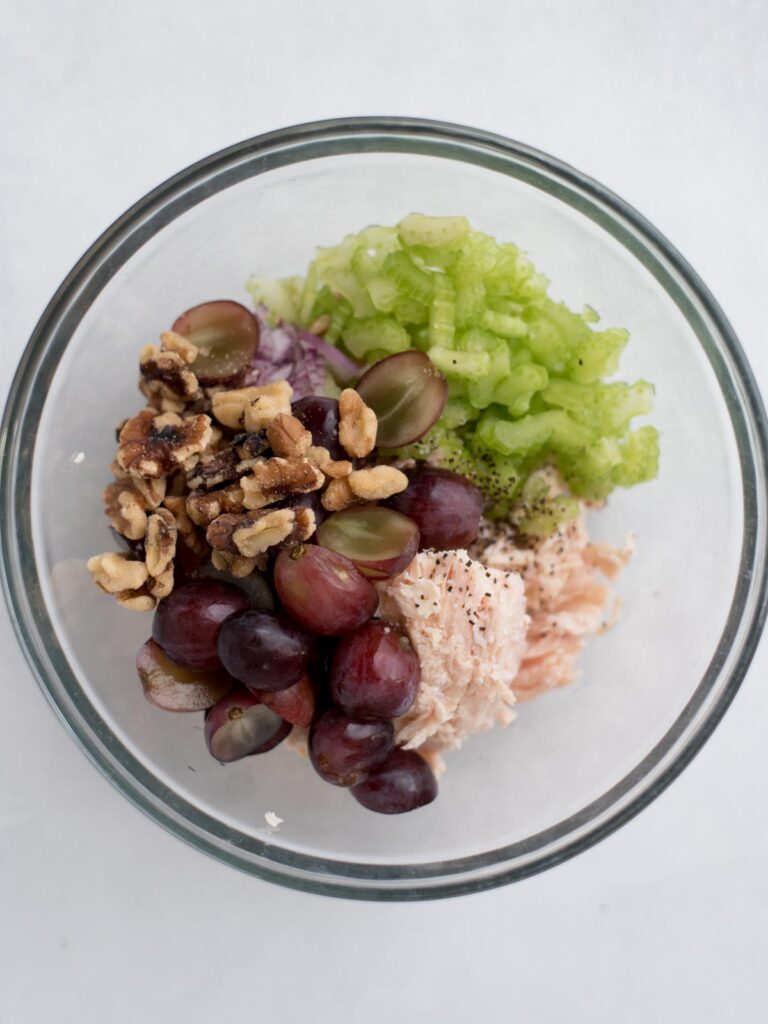 Veggies, grapes, and nuts added to a mixing bowl for preparing chicken salad.