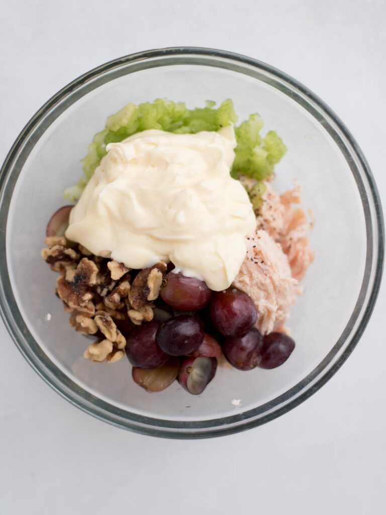 Mayonnaise added to the chicken salad ingredients in a mixing bowl.