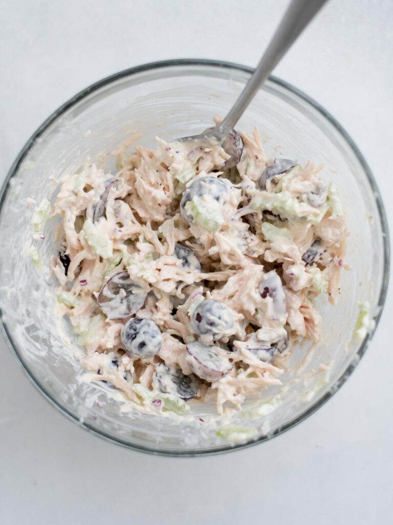 Chicken salad in a glass mixing bowl with a fork resting in it.