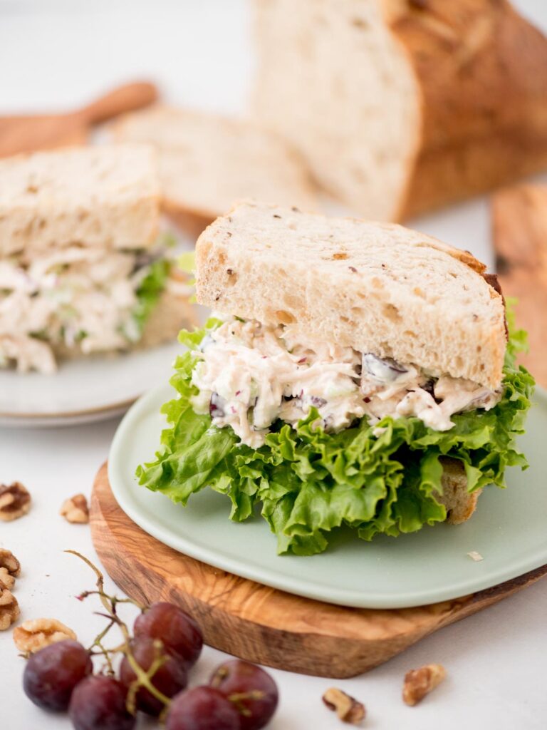 Grapes laying next to a plate with half chicken salad sandwich.